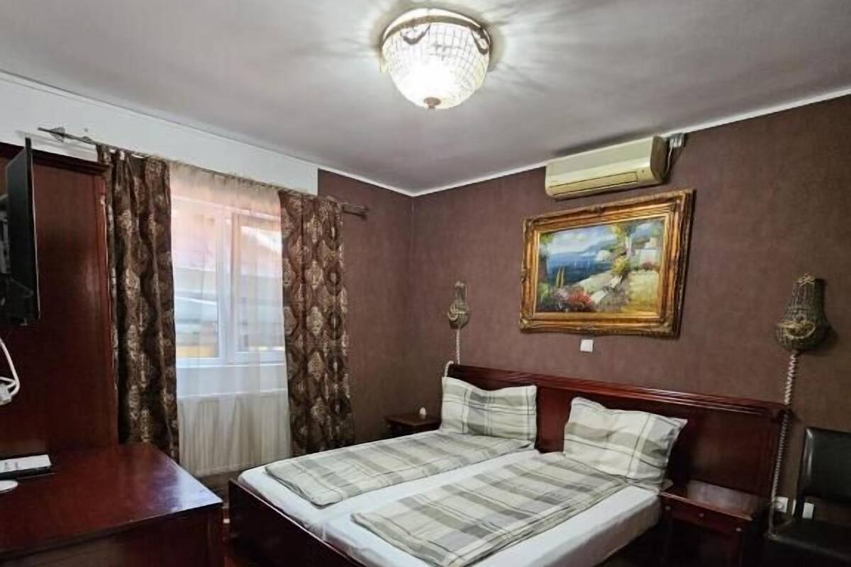 A hotel room with a large bed, a desk, a chair, a painting on the wall, and a patterned carpet.