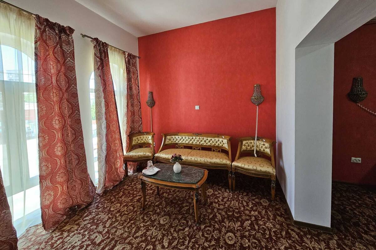 A room with a red wall, patterned curtains, a sofa set, a small table, and two wall-mounted lamps.