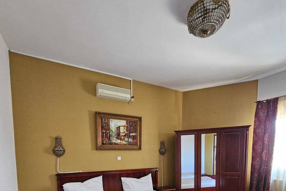 A room with two single beds, a wooden wardrobe, a painting on the wall, and a ceiling light fixture.