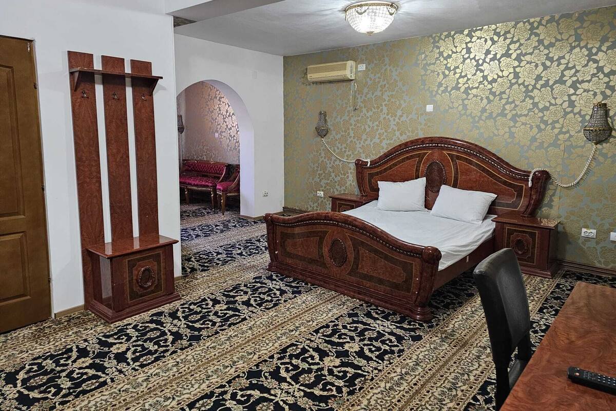A bedroom with a wooden bed, a patterned carpet, a wooden cabinet, and a wall-mounted telephone.