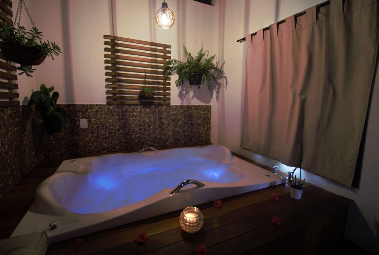 Une salle de spa avec un bain à remous, des lambris en bois, des plantes en pot et une bougie posée sur le sol.