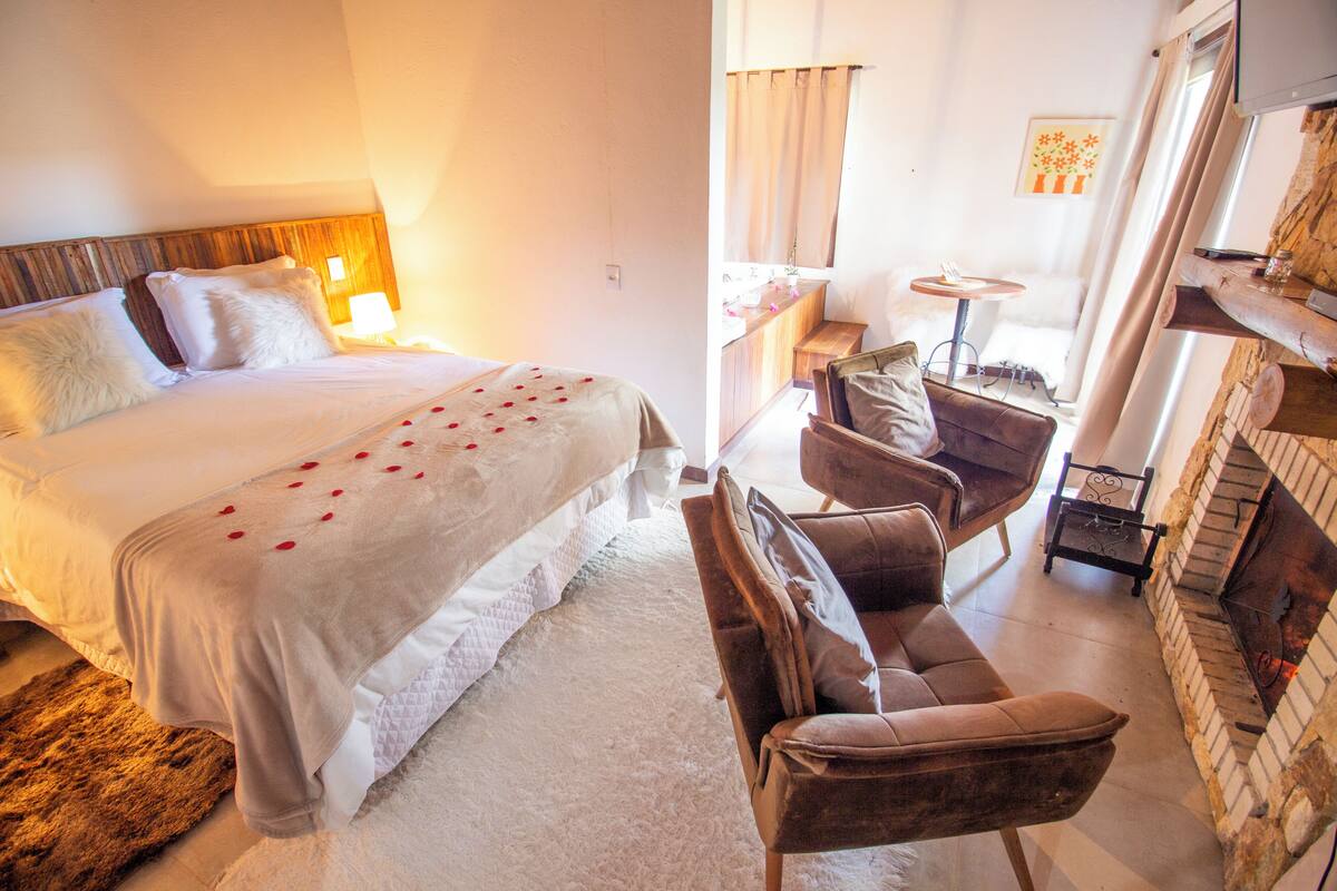Une chambre d’hôtel comprenant un lit, un coin salon avec un fauteuil et une petite table, ainsi qu’une cheminée.