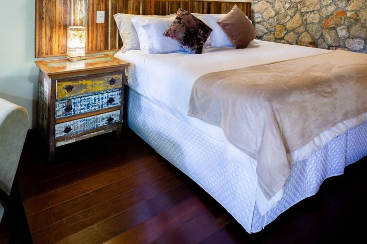 Une chambre à coucher avec une tête de lit en bois, un mur en pierre, une table de chevet avec des tiroirs et un lit avec des oreillers.