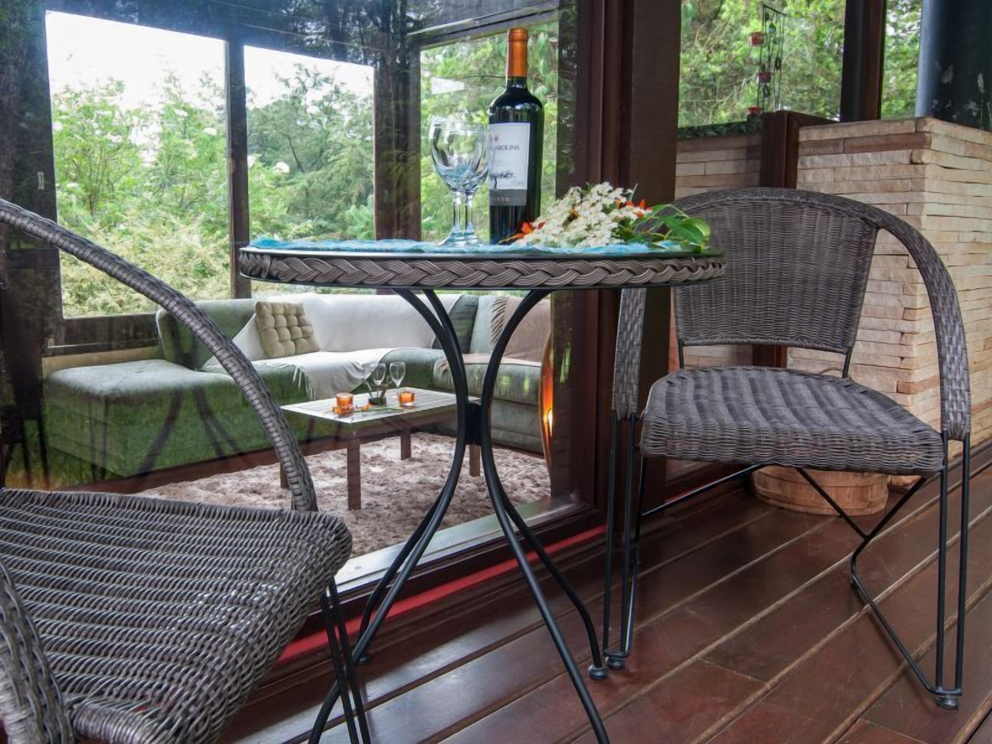 A covered outdoor seating area with wicker chairs, a table with a bottle of wine and glasses, and a sofa.