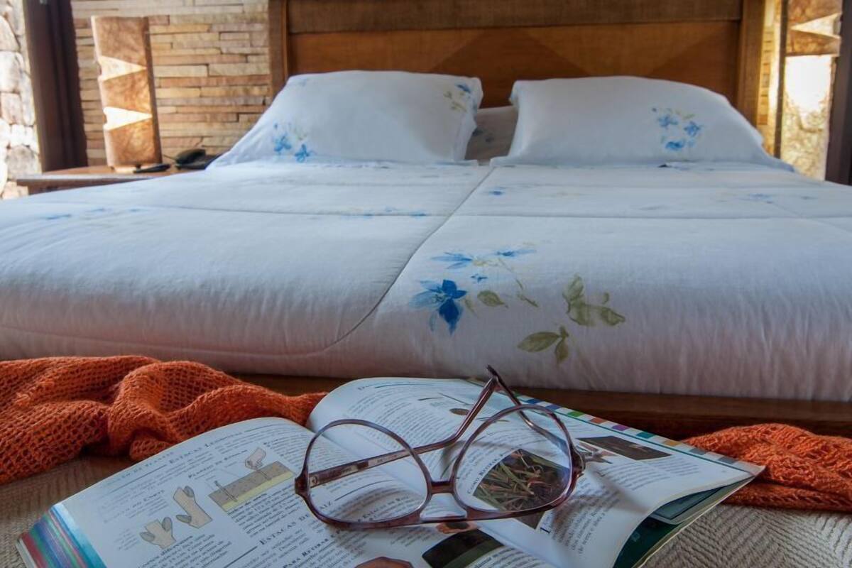 Un lit double avec une literie à motifs floraux, une tête de lit en bois et un mur en briques.