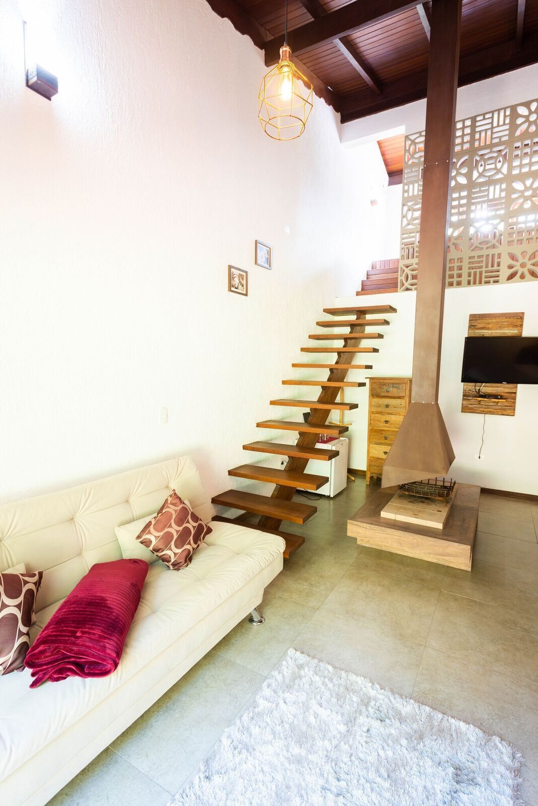 Una sala de estar moderna con un sofá blanco, un cojín rojo, un felpudo blanco y una escalera de madera original.