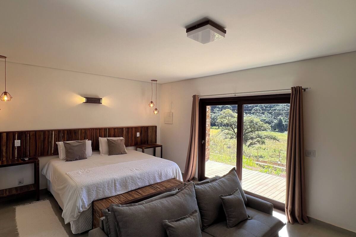 Une chambre avec un grand lit, une tête de lit en bois, un canapé et une vue sur un jardin, accessible par une porte coulissante.