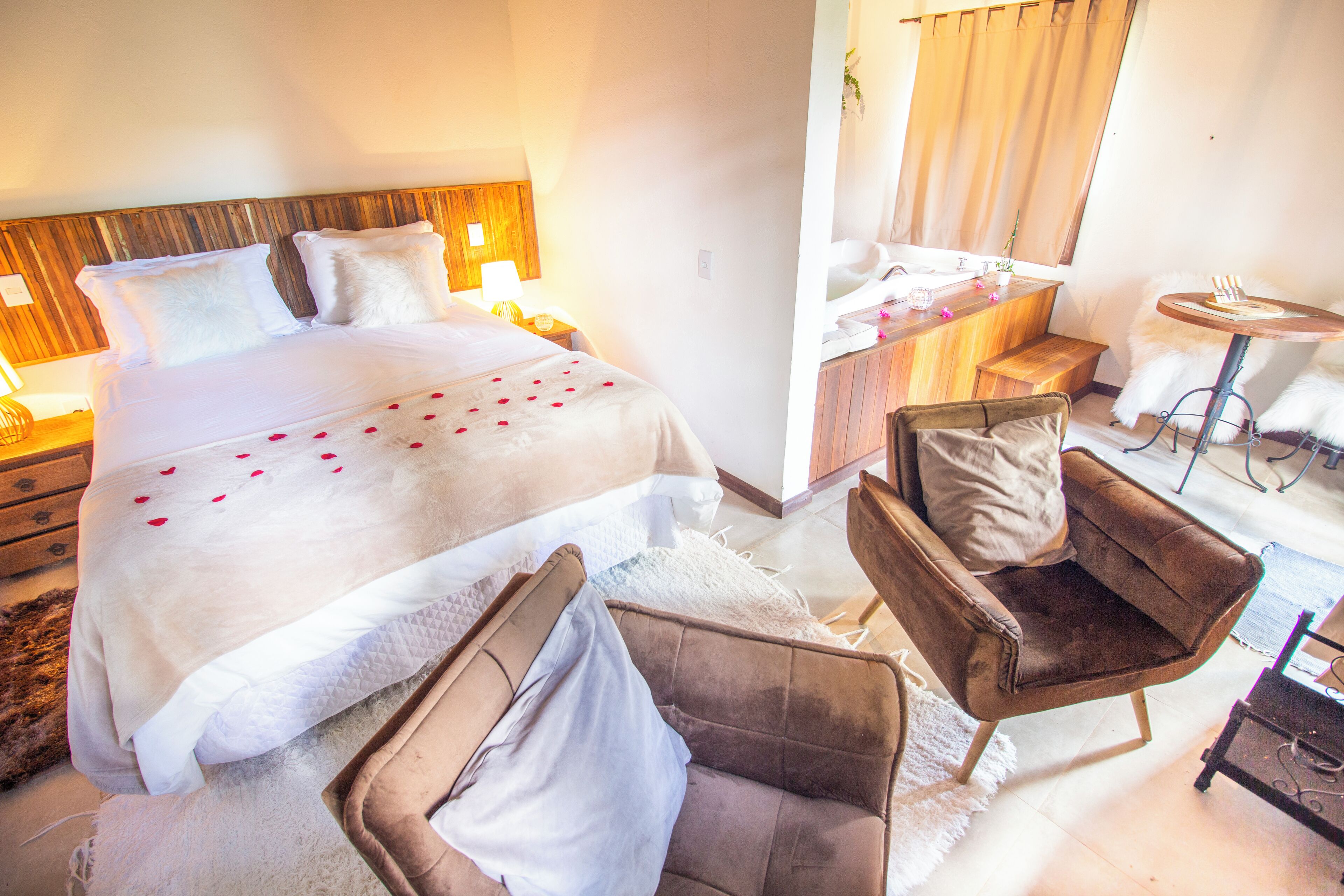Une chambre d’hôtel avec un grand lit, un fauteuil brun, une petite table ronde et une tête de lit en bois.