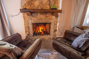 Una sala de estar acogedora con chimenea de piedra, sofás de cuero y un estante de madera sobre la chimenea.