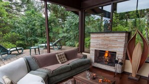 Een moderne woonkamer met een stenen open haard, een grijze bank en uitzicht op een weelderige tuin.