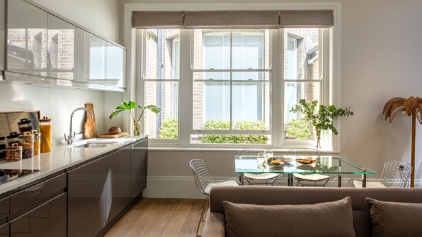 Une cuisine moderne avec une table à manger en verre, un canapé et une grande fenêtre donnant sur un paysage verdoyant.