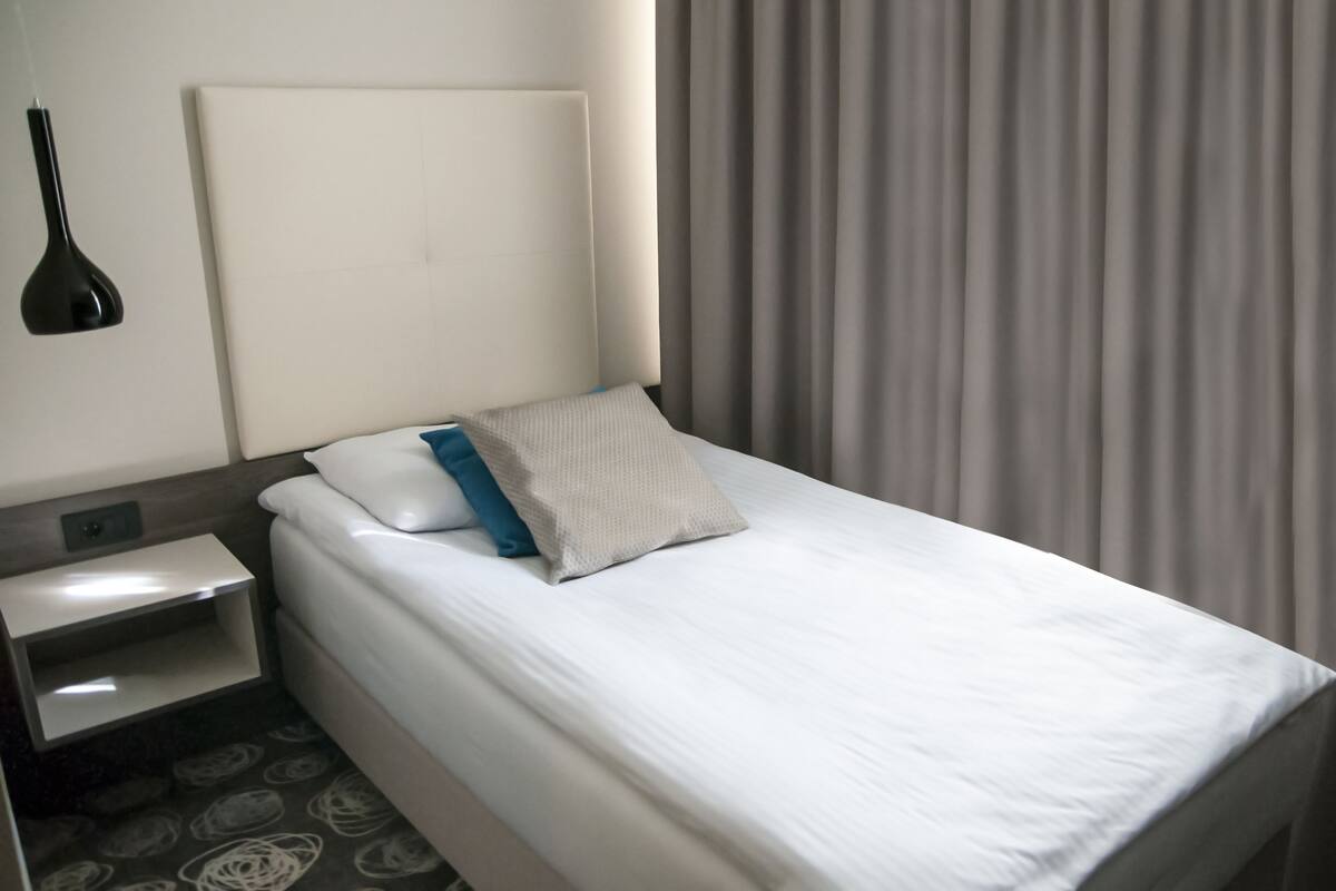 Una habitación de hotel con una cama bien hecha, una mesita de noche y una lámpara.