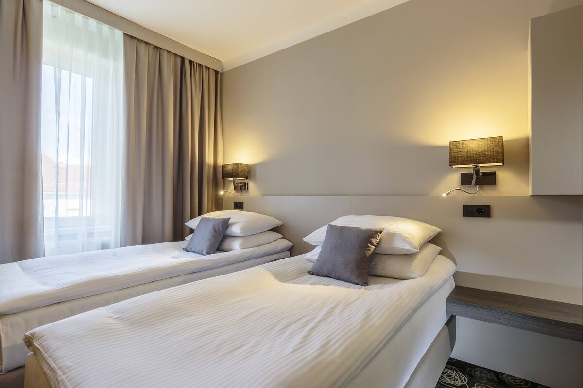 Una habitación de hotel con dos camas, un ventanal con cortinas y lámparas fijadas a la pared.