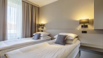 A hotel room with two beds, a large window with curtains, and wall-mounted lamps.
