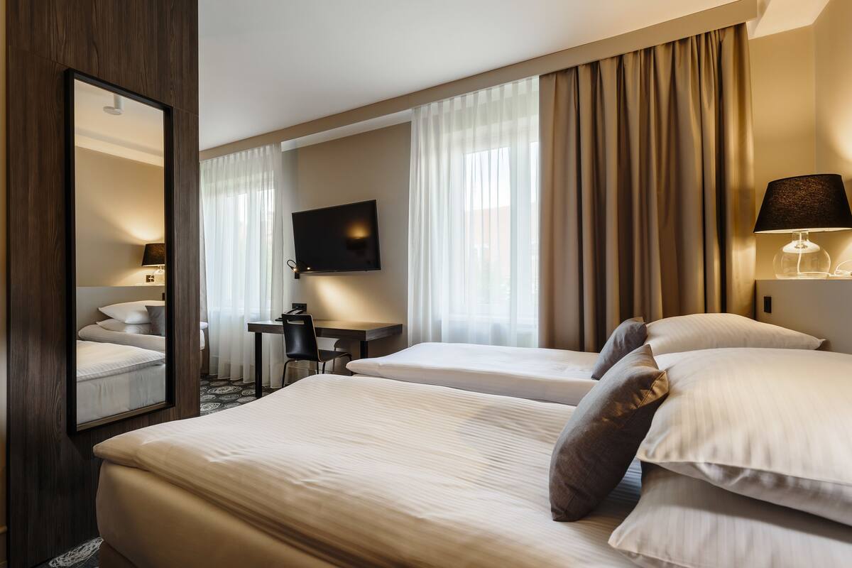Una habitación de hotel con dos camas, un escritorio, una silla, un televisor y una lámpara.