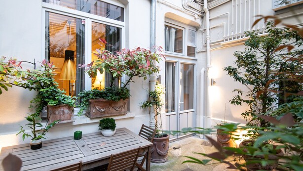 A courtyard with a wooden table and chairs, potted plants, and a window with a hanging light fixture. - MHL - Maison Hotel Lyon (Lyon)