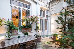 Een binnentuin met een houten tafel en stoelen, plantenpotten en een raam met een hanglamp.