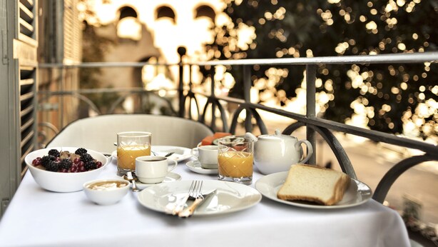 A breakfast table with a bowl of berries, a glass of orange juice, a cup, a teapot, and a slice of toast. - The Shire Hotel (Rome)