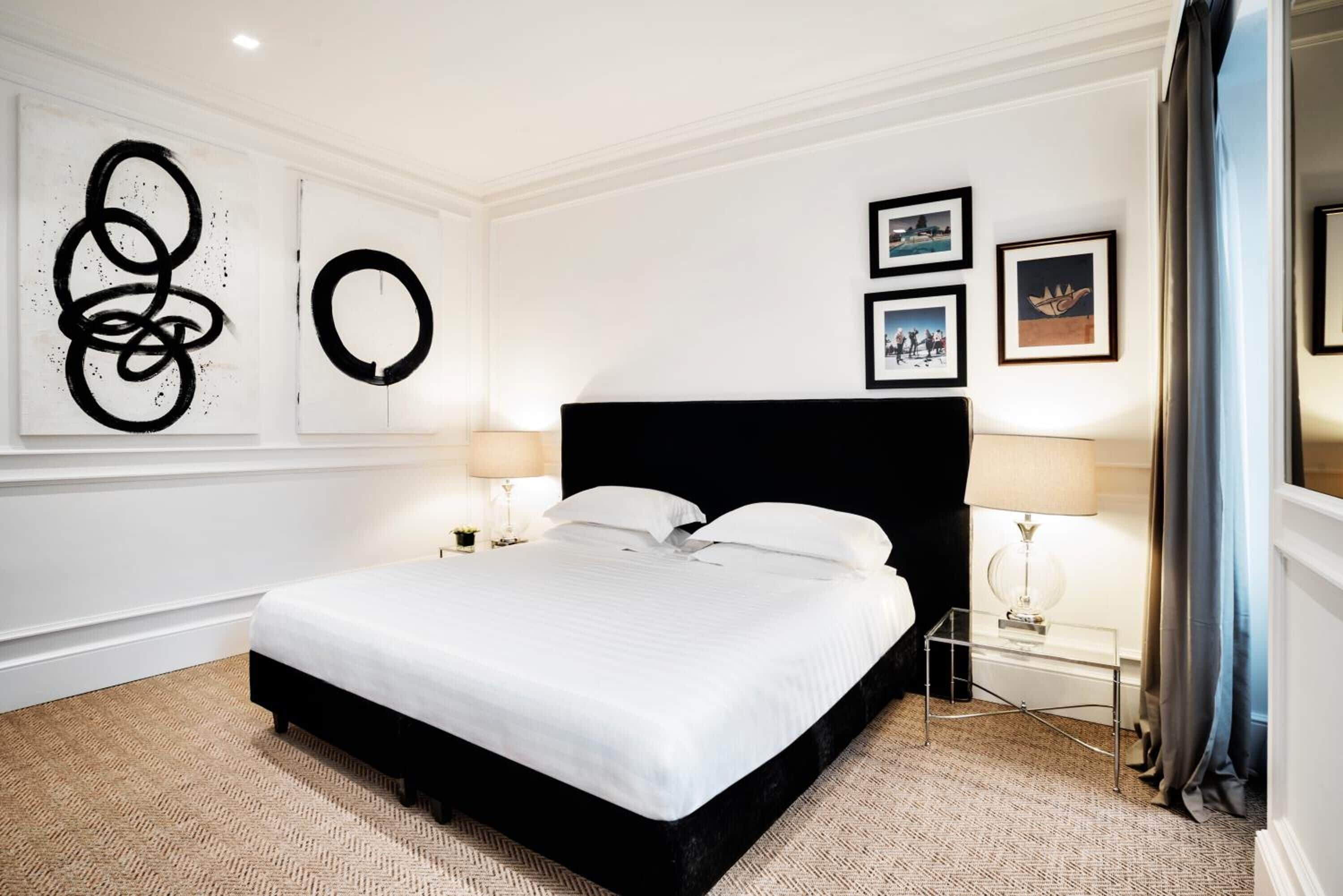 Ein Hotelzimmer mit einem großen Bett, zwei Nachttischen mit Lampen, einem schwarzen Kopfteil und abstrakter Wandkunst.