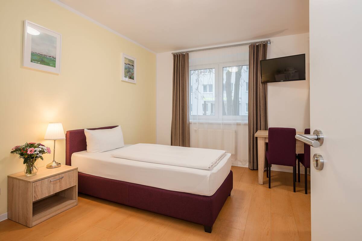 Habitación de hotel con cama, escritorio, silla, televisión y ventana con cortinas.