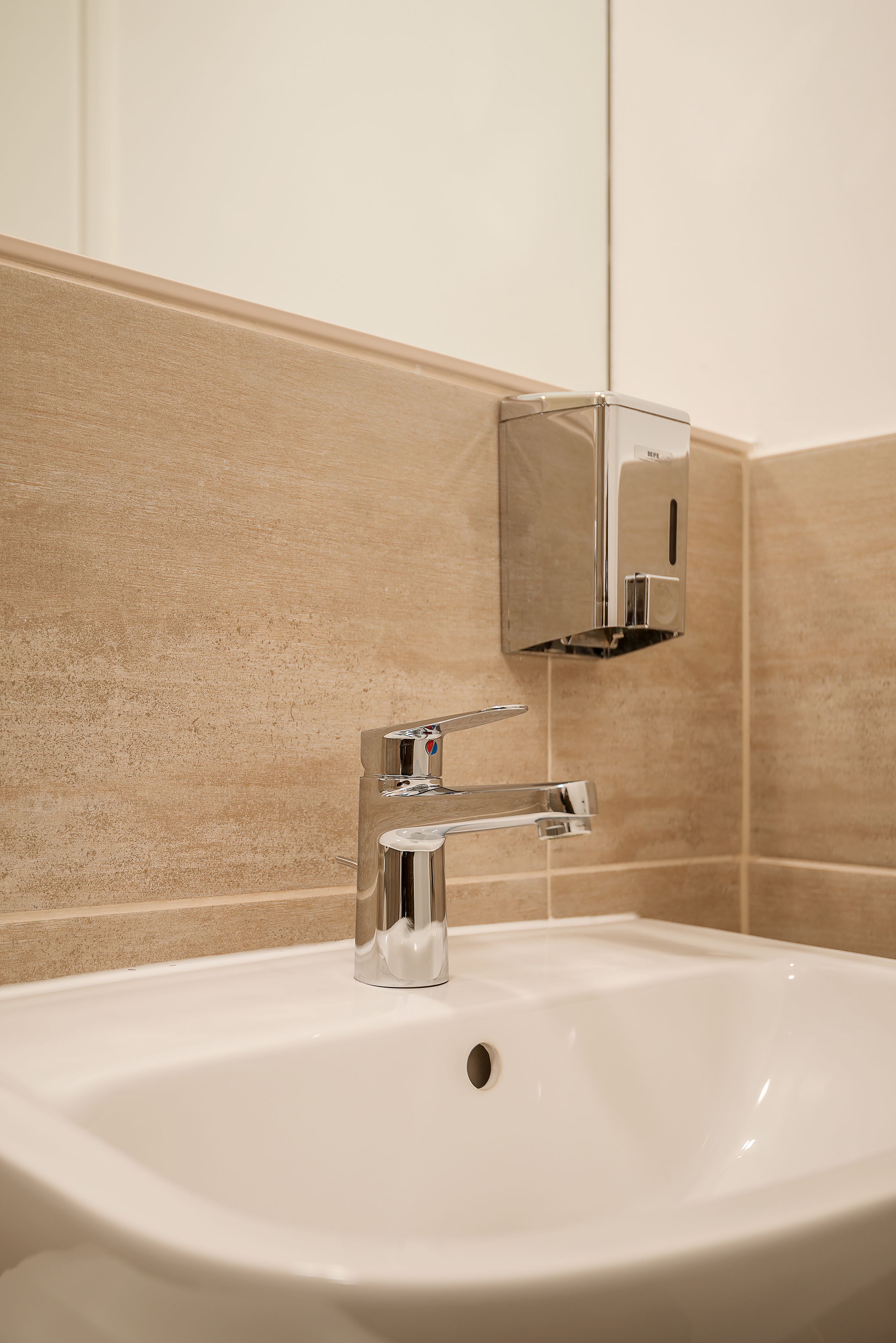 A bathroom sink with a chrome faucet and a soap dispenser mounted on the wall.