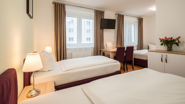 A hotel room with two beds, a desk, a chair, a TV, and a window with curtains. - Hotel City Green Berlin (Berlin)
