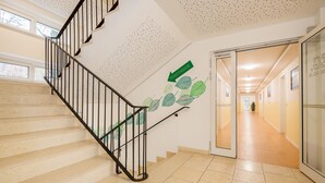 A staircase with a black railing, beige steps, and a wall with a green arrow pointing downwards. - Hotel City Green Berlin (Berlin)