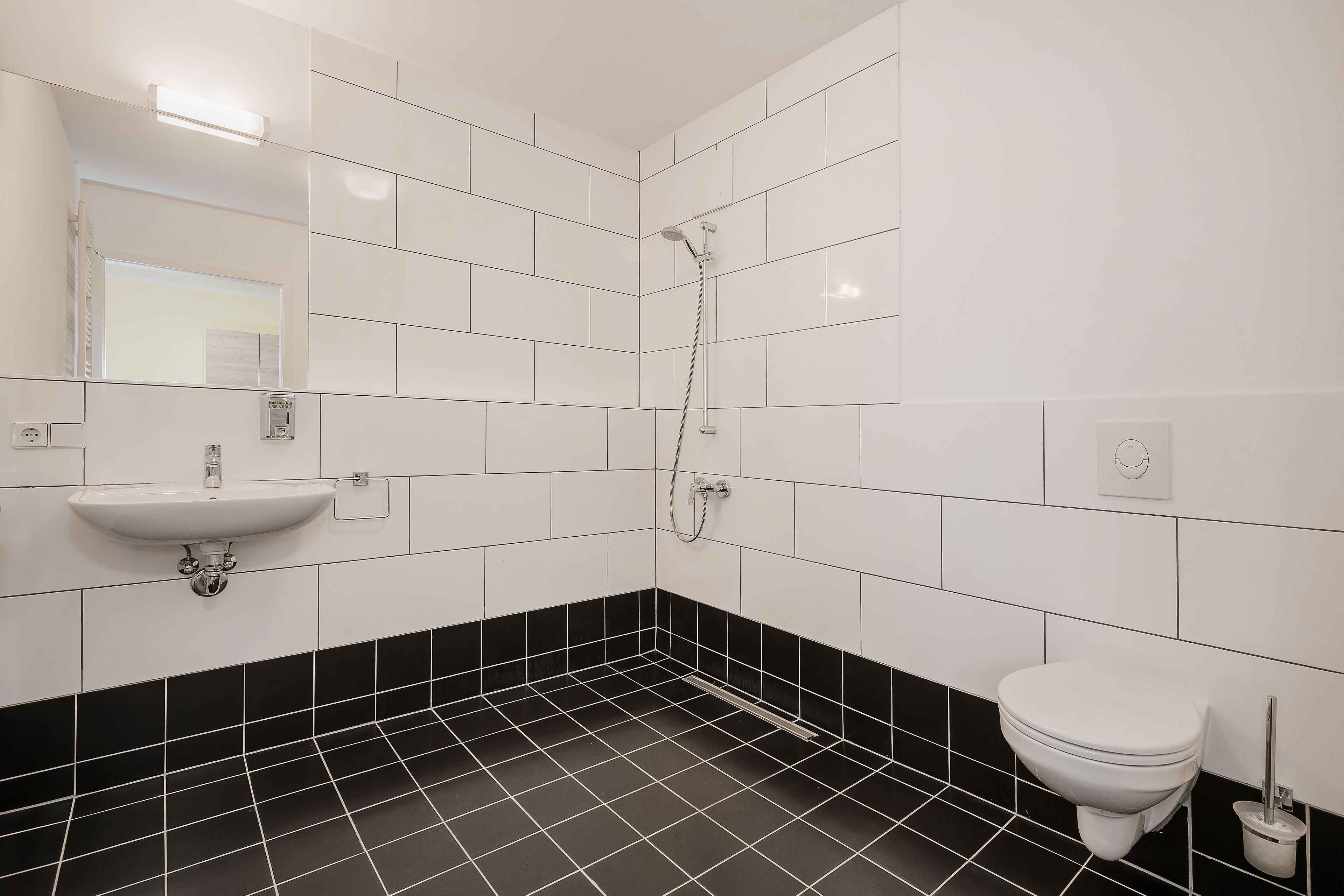 Ein Badezimmer mit weißen und schwarzen Fliesen, einem Waschbecken, einer Toilette und einer Dusche.