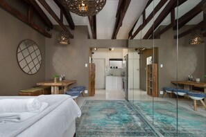 A modern hotel room with a large bed, a blue patterned rug, wooden furniture, and a kitchen area visible through a glass door. - Sandringham 50 - Adults Only (Cape Town)