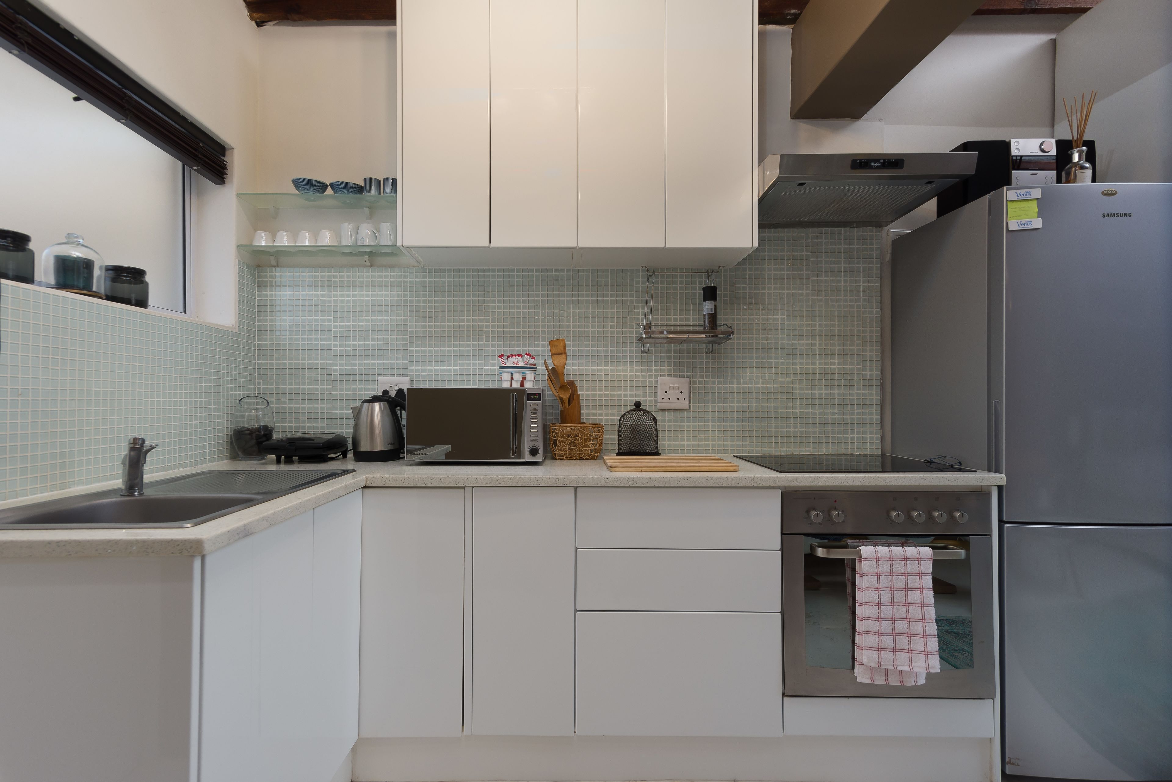 A kitchen with white cabinets, a stainless steel sink, a microwave, a toaster, and a refrigerator.