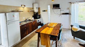 A rustic kitchen with wooden beams, a dining table with chairs, a refrigerator, and a microwave.