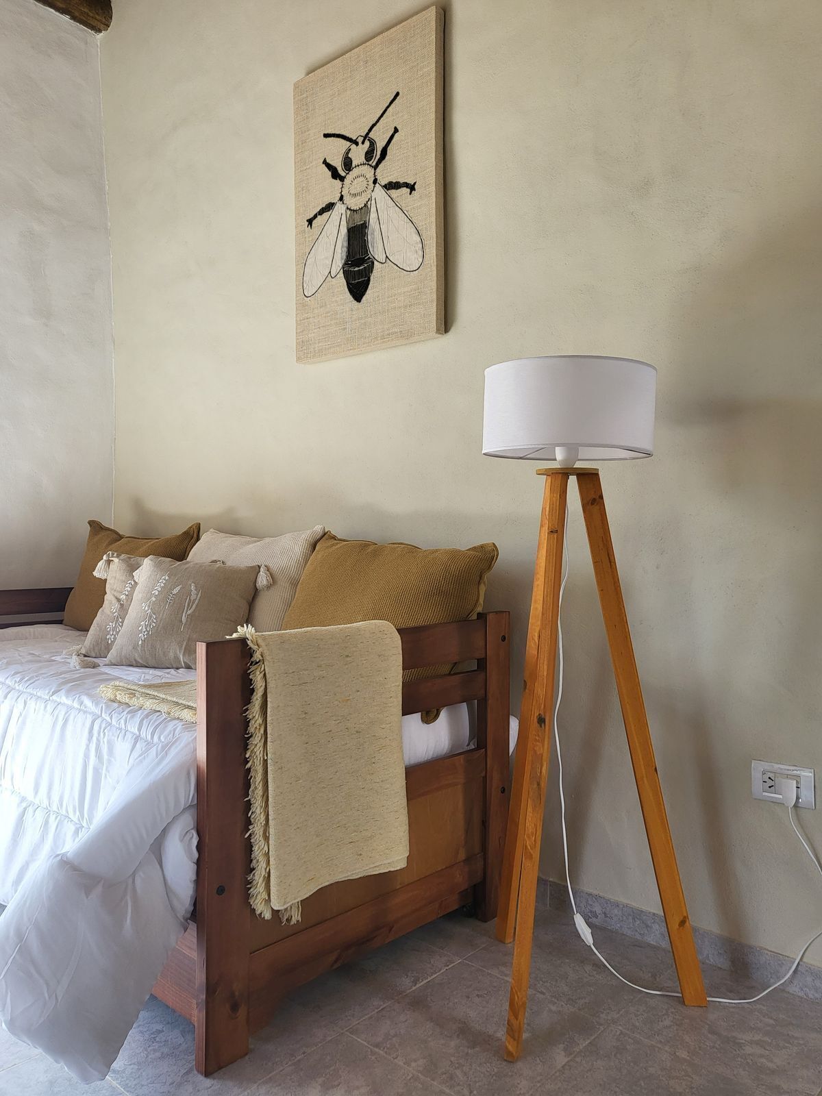 Ein Schlafzimmer mit einem hölzernen Bett, einer Nachttischlampe und einer Insektenillustration an der Wand.