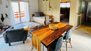 A spacious living area with a wooden ceiling, a dining table with chairs, a sofa, and a large window with curtains.