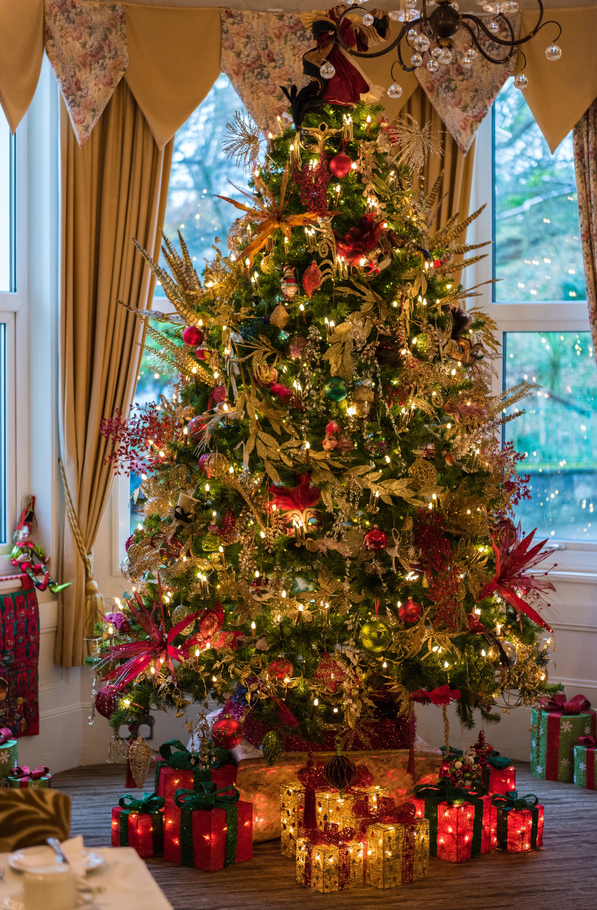Un sapin de Noël décoré de guirlandes lumineuses et d’ornements, entouré de cadeaux emballés.