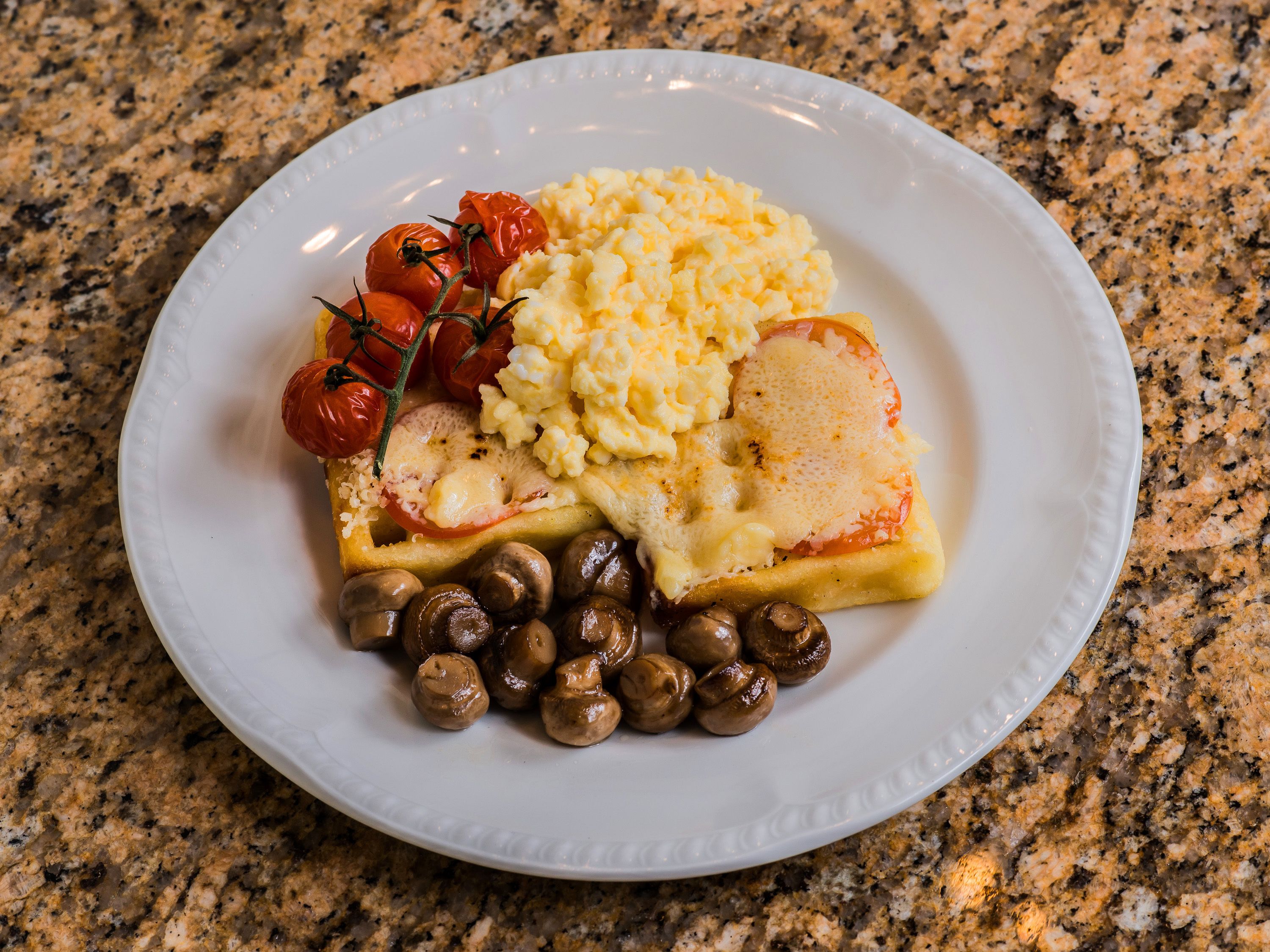 A plate with scrambled eggs, a slice of tomato, a slice of cheese, and mushrooms.