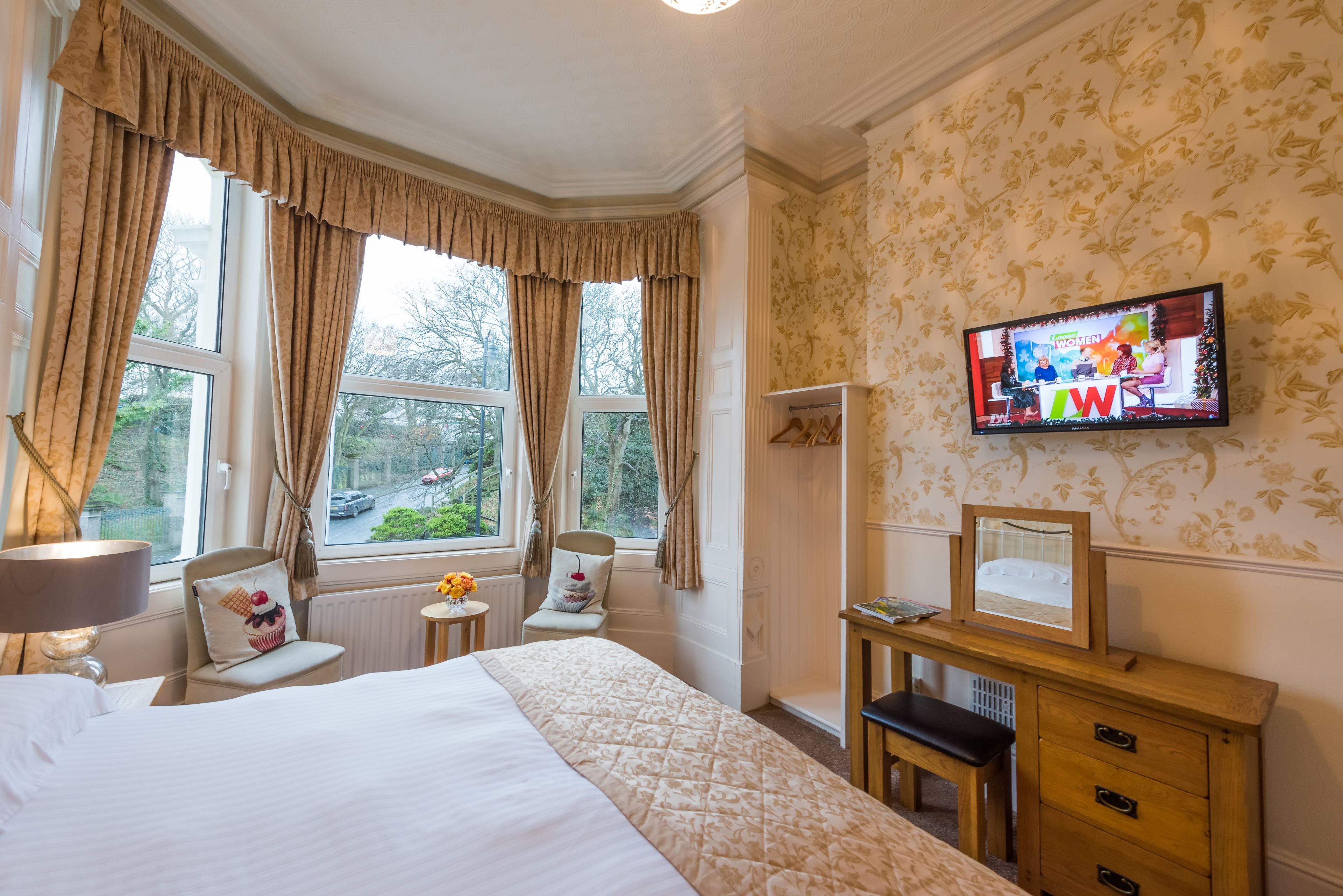Habitación de hotel con una cama grande, un escritorio con espejo, televisión y vistas al exterior a través de las ventanas.