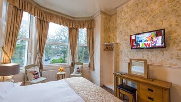Habitación de hotel con una cama grande, un escritorio con espejo, televisión y vistas al exterior a través de las ventanas.