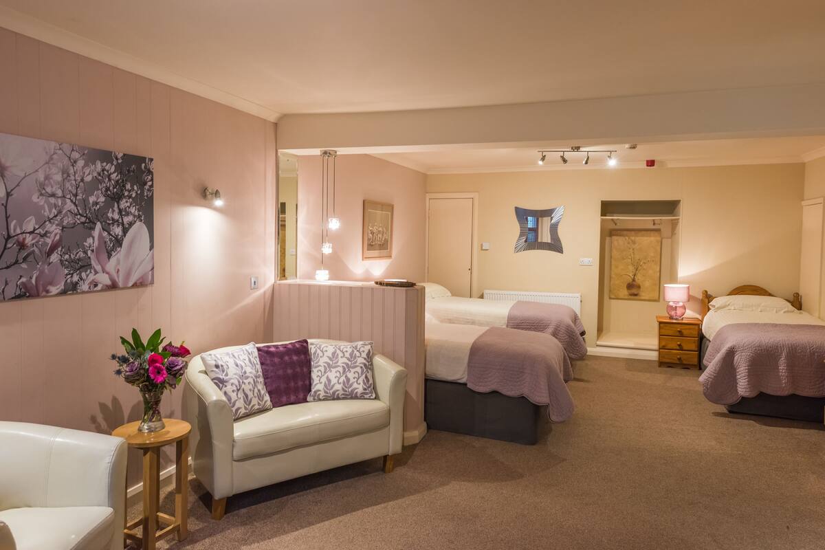 Une chambre avec deux lits, un coin salon avec un canapé et une table de chevet avec une lampe.