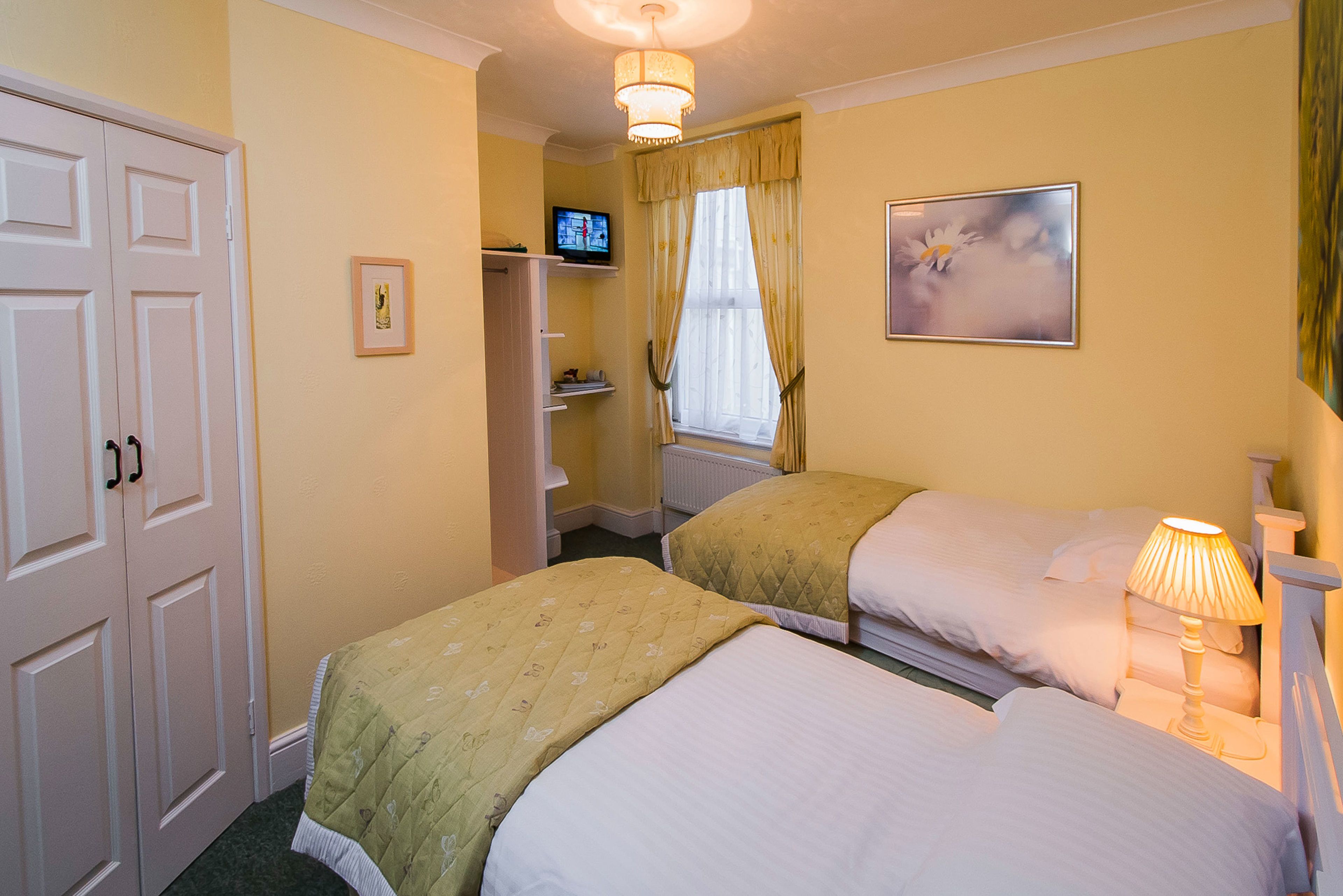 Quarto de hotel com duas camas, televisão, janela com cortinas, um quadro e uma luminária.