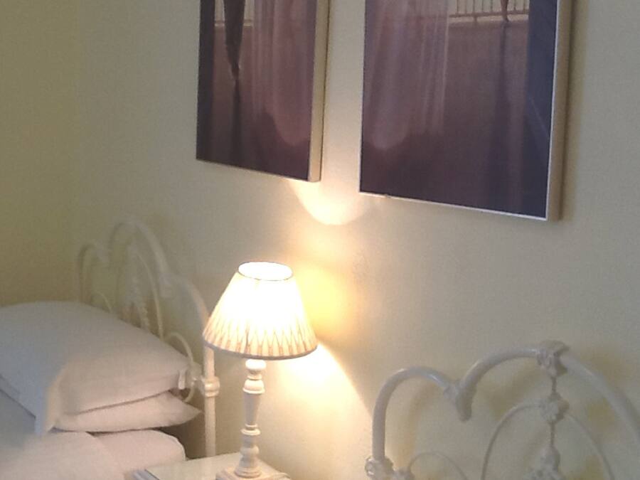 A hotel room with two beds, a nightstand with a lamp, and two paintings on the wall.