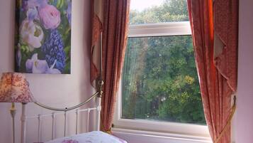 Un dormitorio con cama, mesita de noche, lámpara, ventana con cortinas y un cuadro en la pared.