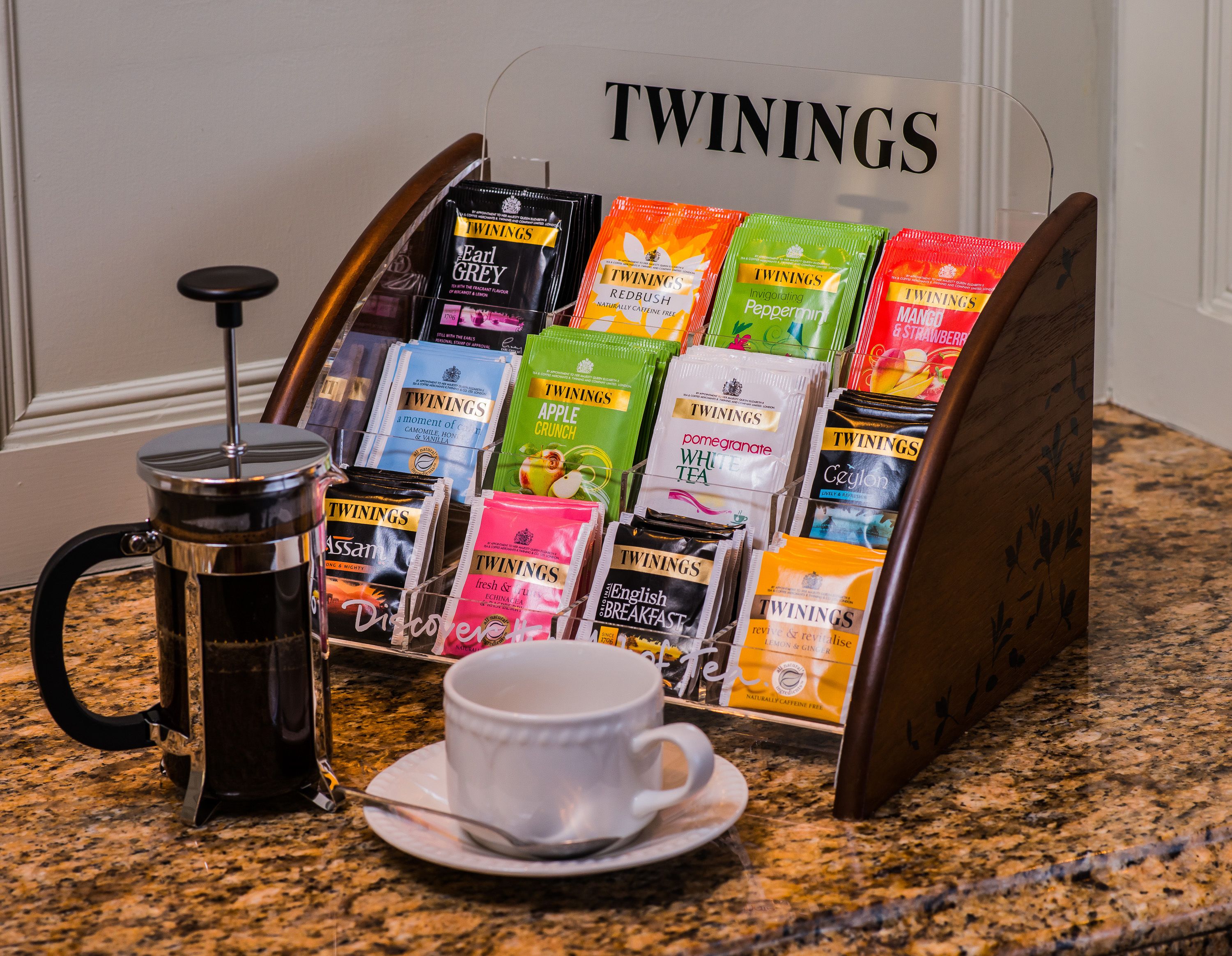 A coffee station with a French press and a display of Twinings tea bags.