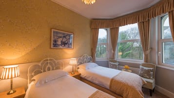 A bedroom with two beds, a chandelier, a window with curtains, and a painting on the wall.