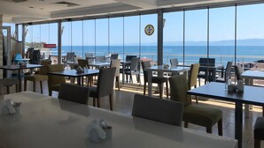A restaurant with tables and chairs arranged near large windows offering a view of the sea. - Sinopark Otel (Sinop)
