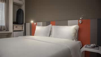 A neatly made bed with white linens, a bedside table with a book and headphones, and a hanging coat rack.