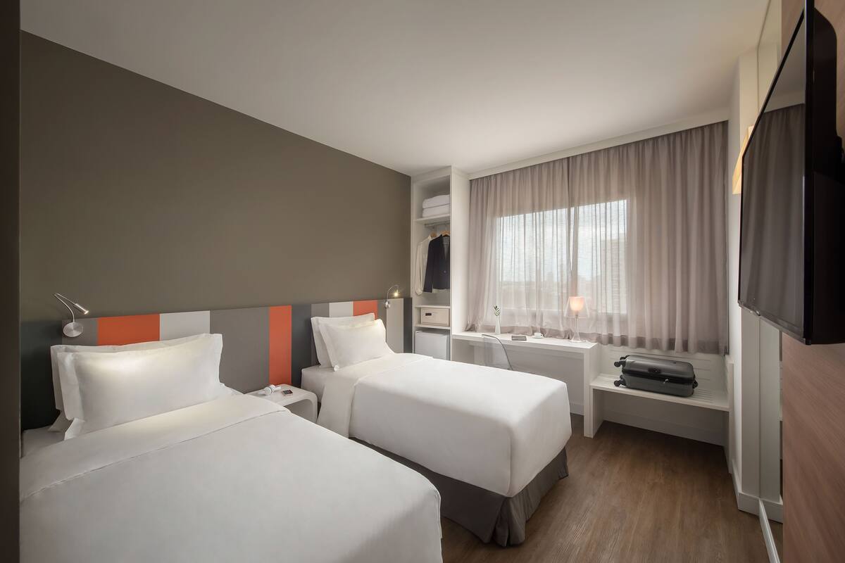Ett hotellrum med två sängar, ett skrivbord, en TV och ett fönster med gardiner.