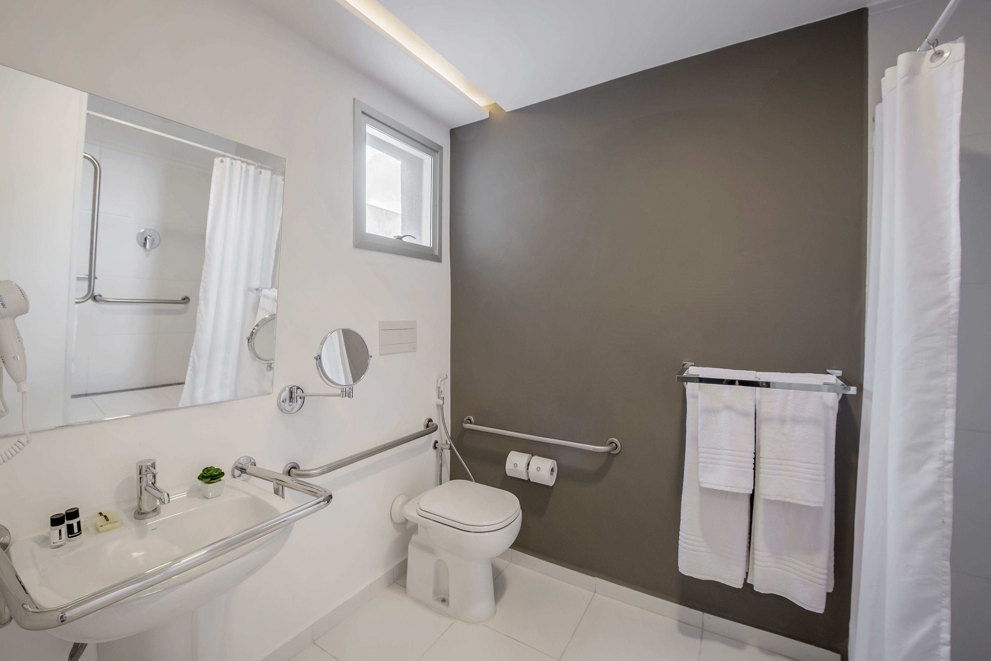 A modern bathroom with a white sink, a toilet, a shower with a grab bar, and a towel rack.