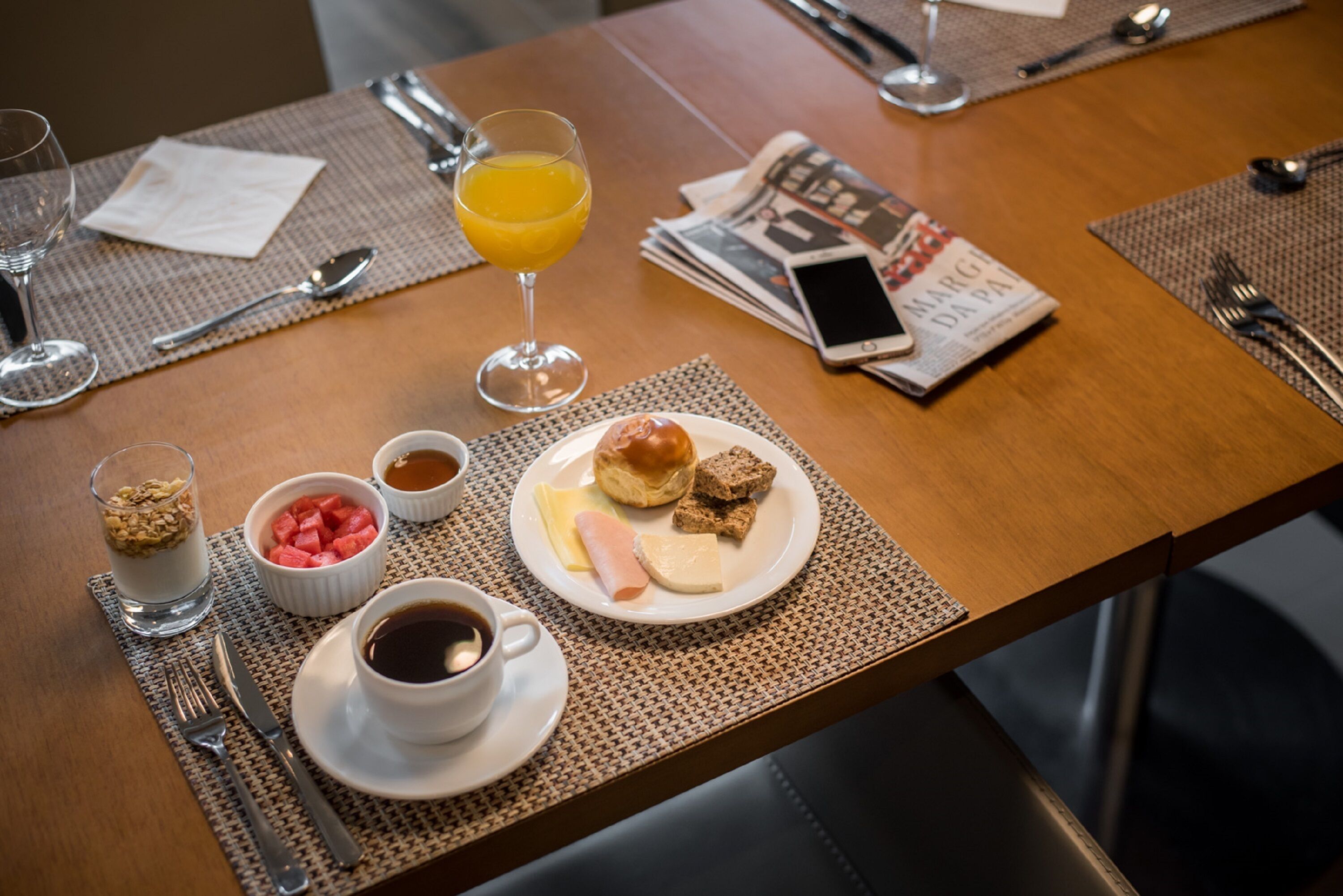 Una escena de desayuno con un plato de comida, un vaso de jugo de naranja y un periódico sobre una mesa de madera.
