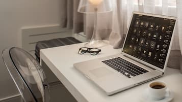 Un ordinateur portable sur un bureau blanc, avec une tasse de café, une paire de lunettes et une lampe.