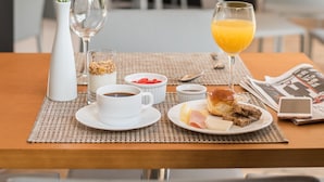 Une table mise pour le petit-déjeuner, avec une place pour deux personnes, comprenant un verre de jus d’orange, une tasse de café, une assiette avec des œufs et des toasts, et un petit vase avec une plante.